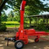 Red agricultural baler-like machine on a dirt yard with a vertical chute and trailer wheels, ready for use on a farm