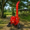 Red portable wood chipper on a trailer in a grassy yard with trees and a shed nearby, ready for use.