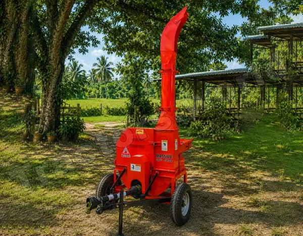 Red portable wood chipper on a trailer in a grassy yard with trees and a shed nearby, ready for use.