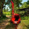 Red wood chipper/shredder on a stand in a sunny garden, with trees and a shed in the background.