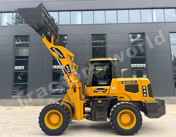 Yellow heavy-duty telehandler with a raised bucket attachment in front of a dark gray office building; brand name MASSIVE visible on the arm.