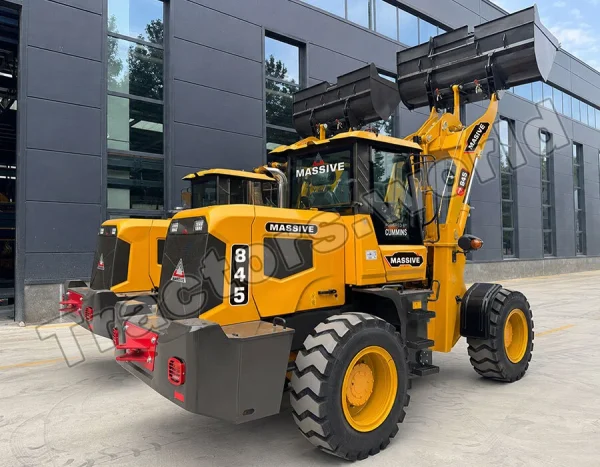 Yellow wheel loader with a raised bucket labeled MASSIVE, parked in front of a modern gray building.