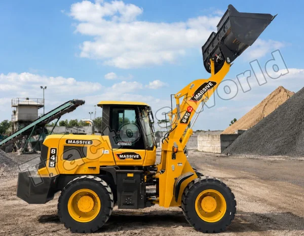 Yellow telehandler loader at a quarry raises its front bucket to move gravel with piles and conveyors in the background
