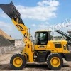 Yellow front-end loader with raised bucket loading gravel at a quarry, clear blue sky in the background and a conveyor belt nearby.
